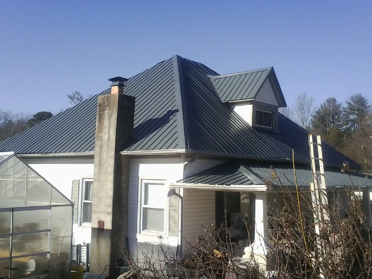 Dark blue standing seam metal roof on a white farmhouse with dormer — Slate & Tile Roof Repair by Roofing Brothers in Elmwood Park