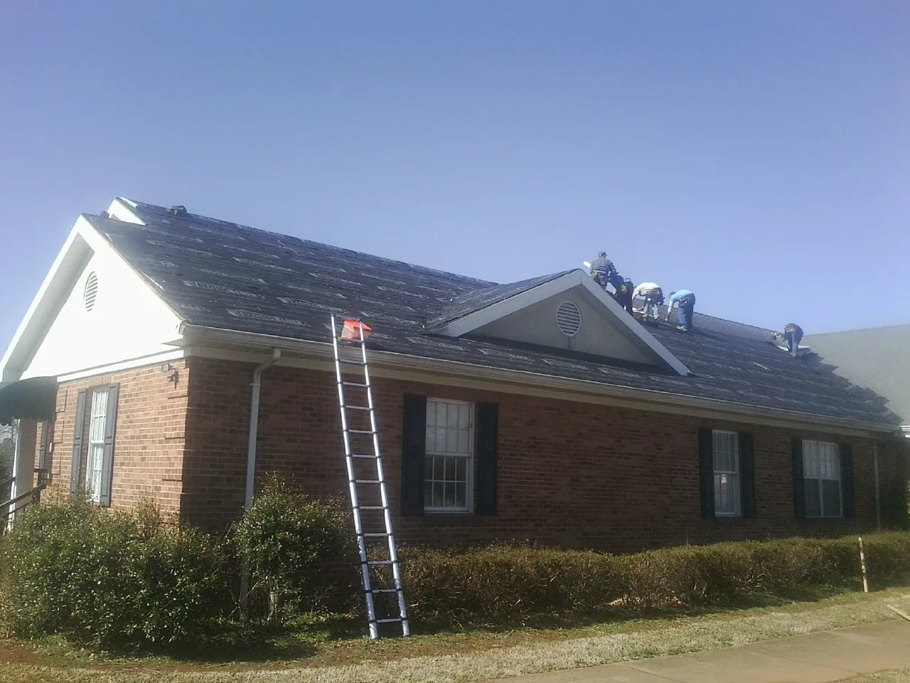 Crew tearing shingles off a brick ranch roof with a ladder set — Metal Roof Repair work by our crew in Elmwood Park