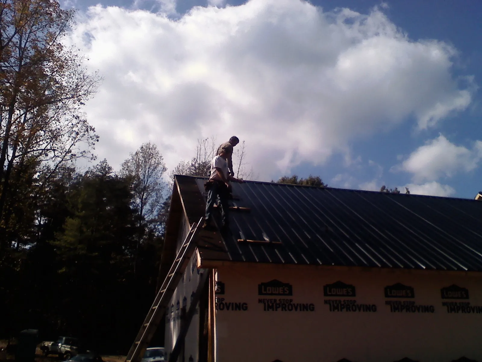 Roofer fastening dark metal panels high against a cloudy sky, from a Roof Inspection job in Elmwood Park