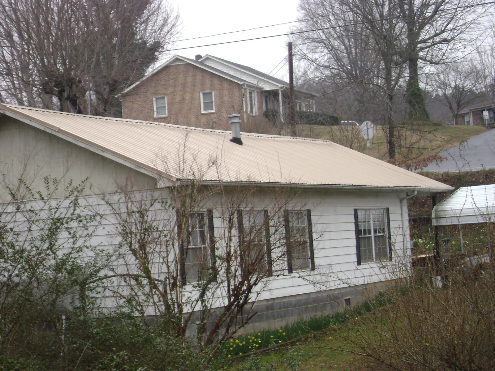 Tan metal roof on a white sided house set into a hillside — Commercial Roofing by Roofing Brothers in Elmwood Park